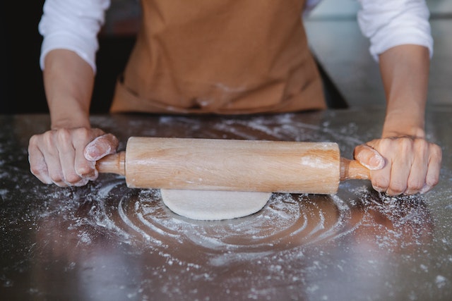 baker rolling own dough on floured surface